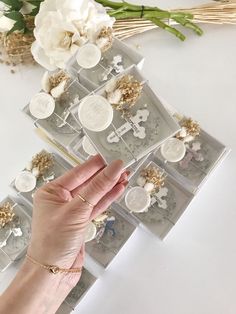 a hand is holding several cards with white flowers in the background and gold accents on them