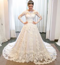 a woman standing in front of a window wearing a white wedding dress with long sleeves