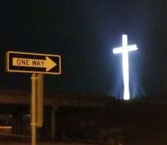 a street sign that is next to a cross on the side of a road at night