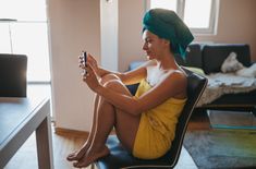 a woman sitting on top of a chair in front of a desk holding a cell phone