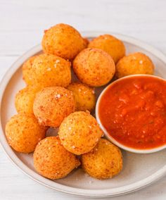 a white plate topped with fried food next to a small bowl of tomato dipping sauce