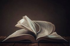 an open book sitting on top of a wooden table in front of a dark background