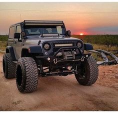 a jeep is parked on the side of a dirt road in front of an orange sunset