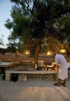 a man cooking food on top of a wooden table next to a large rock wall