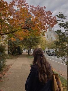 a woman walking down a sidewalk next to trees