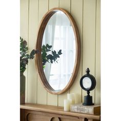 a round mirror sitting on top of a wooden dresser next to a clock and potted plant