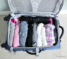 an open suitcase filled with clothes on top of carpeted floor next to white walls