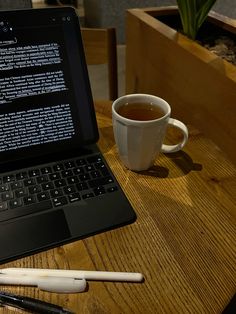 a laptop computer sitting on top of a wooden table next to a cup of coffee