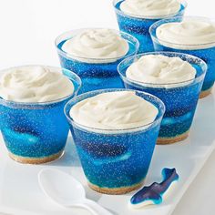 six blue dessert cups with white frosting and sprinkles on a tray