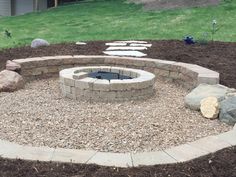 an outdoor fire pit surrounded by rocks and mulch in the middle of a yard