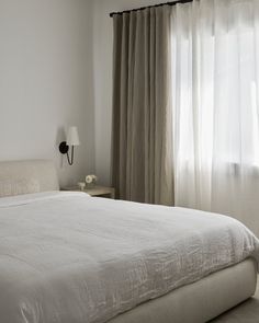 a white bed sitting next to a window covered in curtains