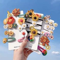 a person holding up a bunch of hair clips with flowers on them in front of a blue sky