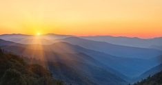 the sun is setting in the mountains with trees on each side and hills to the left