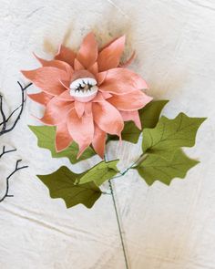 a paper flower and leaves on a white surface with branches in the foreground, and another piece of art that appears to have been made out of paper