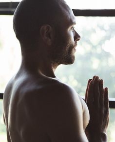 a man standing in front of a window with his hands clasped to his chest and praying