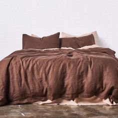 an unmade bed with brown linens and pillows on the bottom, in front of a white wall