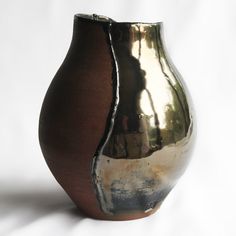 a brown and silver vase sitting on top of a white table