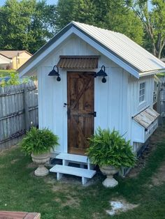 a small white shed sitting on top of a lush green field next to a wooden fence