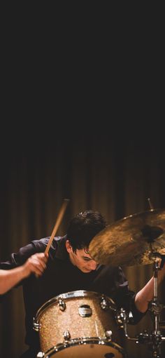 a man is playing drums in front of a dark background with the drum sticks sticking out