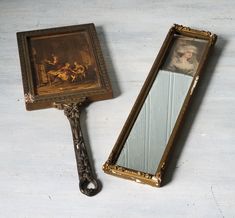 an antique mirror with a painting on it next to a small framed mirror that is sitting on the floor