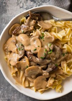 a white bowl filled with pasta covered in mushroom gravy next to a spoon