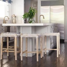 three stools sitting in front of a kitchen island with two vases on it