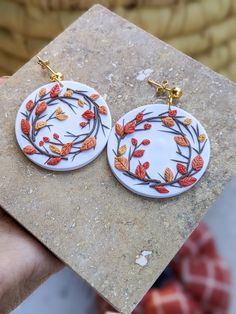 a pair of white and orange earrings with leaves on them sitting on top of a stone slab