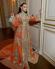 a woman in an orange and gold dress standing on a wooden floor with her arms outstretched