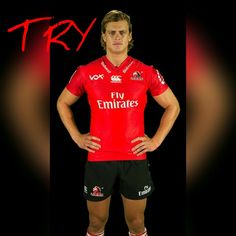 a rugby player poses for the camera in his team's red jersey and black shorts