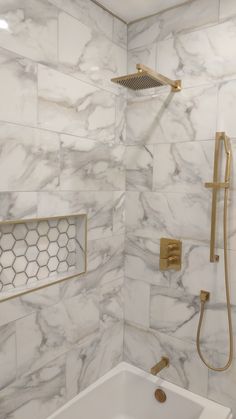 a bathroom with white marble walls and gold fixtures on the shower head, tub, and faucet