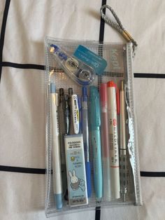 a clear case filled with different types of pens and writing utensils on top of a bed