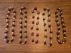 three necklaces are lined up on a wooden surface, one is brown and the other is white