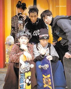 four young men posing with their skateboards in front of a yellow door and orange building