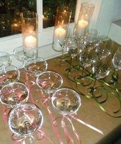 there are many wine glasses on the table with candles in them and some pink ribbons