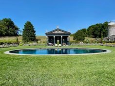 a small pool in the middle of a grassy area with a gazebo and water tower