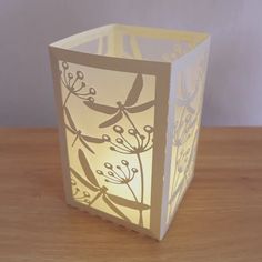 a paper lantern is sitting on top of a wooden table with a white box in the shape of a flower