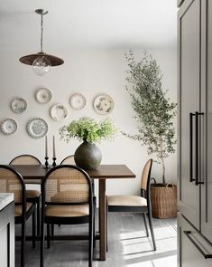 a dining room table with chairs and plates on the wall behind it, along with a vase filled with flowers