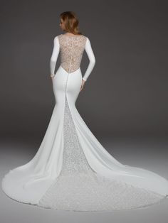 a woman in a white wedding dress with long sleeves and an open back, standing against a