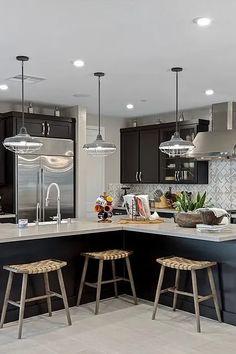 a kitchen with two stools in front of an island and lights above the sink