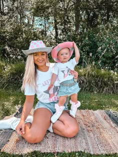 a woman sitting on the ground holding a baby wearing a cowboy hat and blue shorts