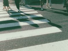 several people walking across a crosswalk in the street with their shadows on the ground