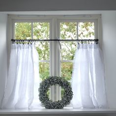 a wreath sits on the window sill in front of two windows with white curtains