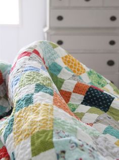 a bed with a quilt on top of it next to a dresser and drawers in a room