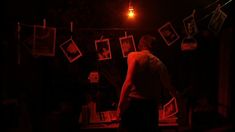 a man standing in front of a dark room with pictures on the wall and lights hanging above him