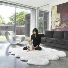 a woman sitting on top of a white rug next to a baby in front of a couch