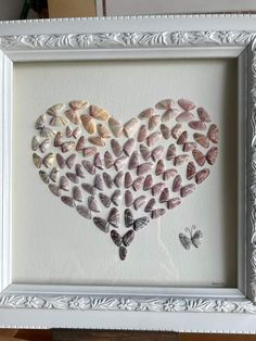 a heart made out of seashells is displayed in a white frame on a table