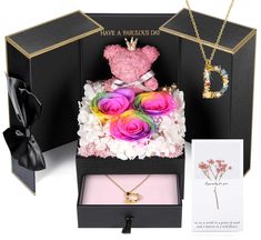 a pink teddy bear sitting on top of a black box next to flowers and a card