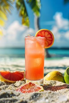 a drink sitting on top of a sandy beach next to watermelon and limes