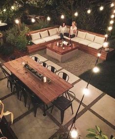 two people sitting at a table in the middle of an outdoor patio with string lights