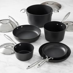 an assortment of pots and pans on a marble counter top with utensils